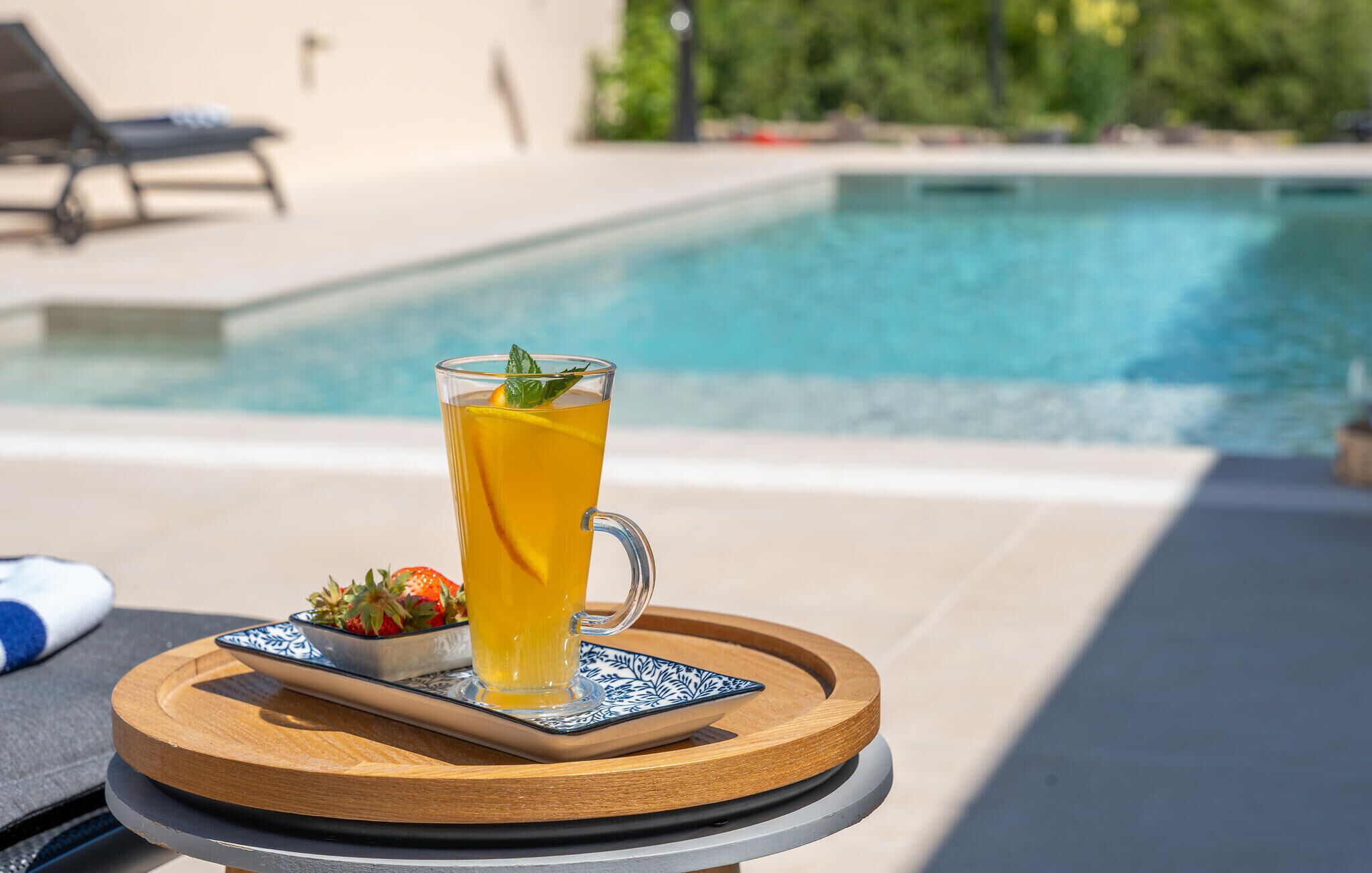 Ein Glas Orangensaft mit Minze auf einem Holztablett am Pool.