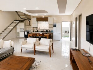 A modern living room with a staircase, a dining area, and a kitchen with white cabinets and stainless steel appliances. - Casa da Lagoa - Marechal Deodoro-AL  (Marechal Deodoro)