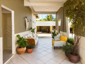 A spacious indoor area with a tiled floor, a sofa, a chair, and potted plants. - Casa da Lagoa - Marechal Deodoro-AL  (Marechal Deodoro)