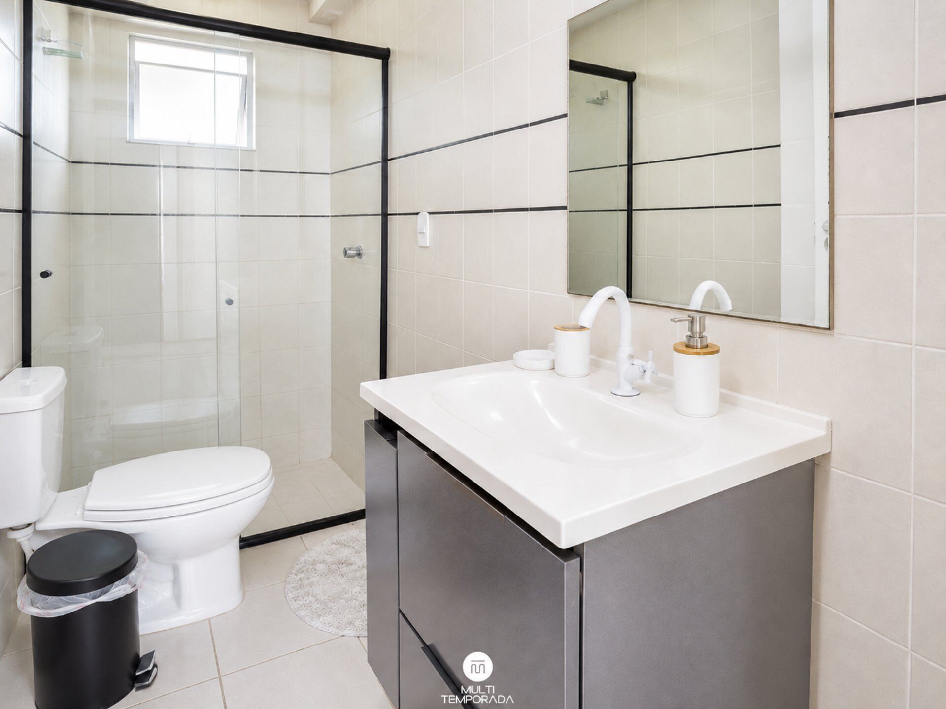 A modern bathroom with a glass-enclosed shower, a white toilet, a sink with a mirror, and a trash bin.