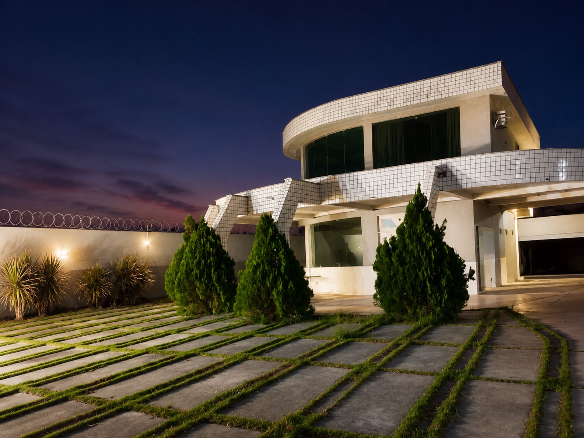 A modern building with a curved facade, large windows, and a well-maintained lawn with geometric patterns.