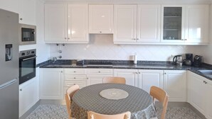 A kitchen with white cabinets, a microwave, an oven, a sink, and a dining table with chairs. - PRAIA DA ROCHA - DOM QUIXOTE (Portimão)
