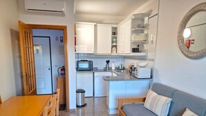 Et kompakt køkken med spiseplads, en sofa og en skraldespand.