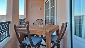 En balkon med et træbord og stole, et vindue med persienner, og en vægmonteret lampe.