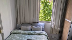 Ein Einzelbett mit einem blumigen Überwurf, zwei Kissen und einem aufgerollten Handtuch.