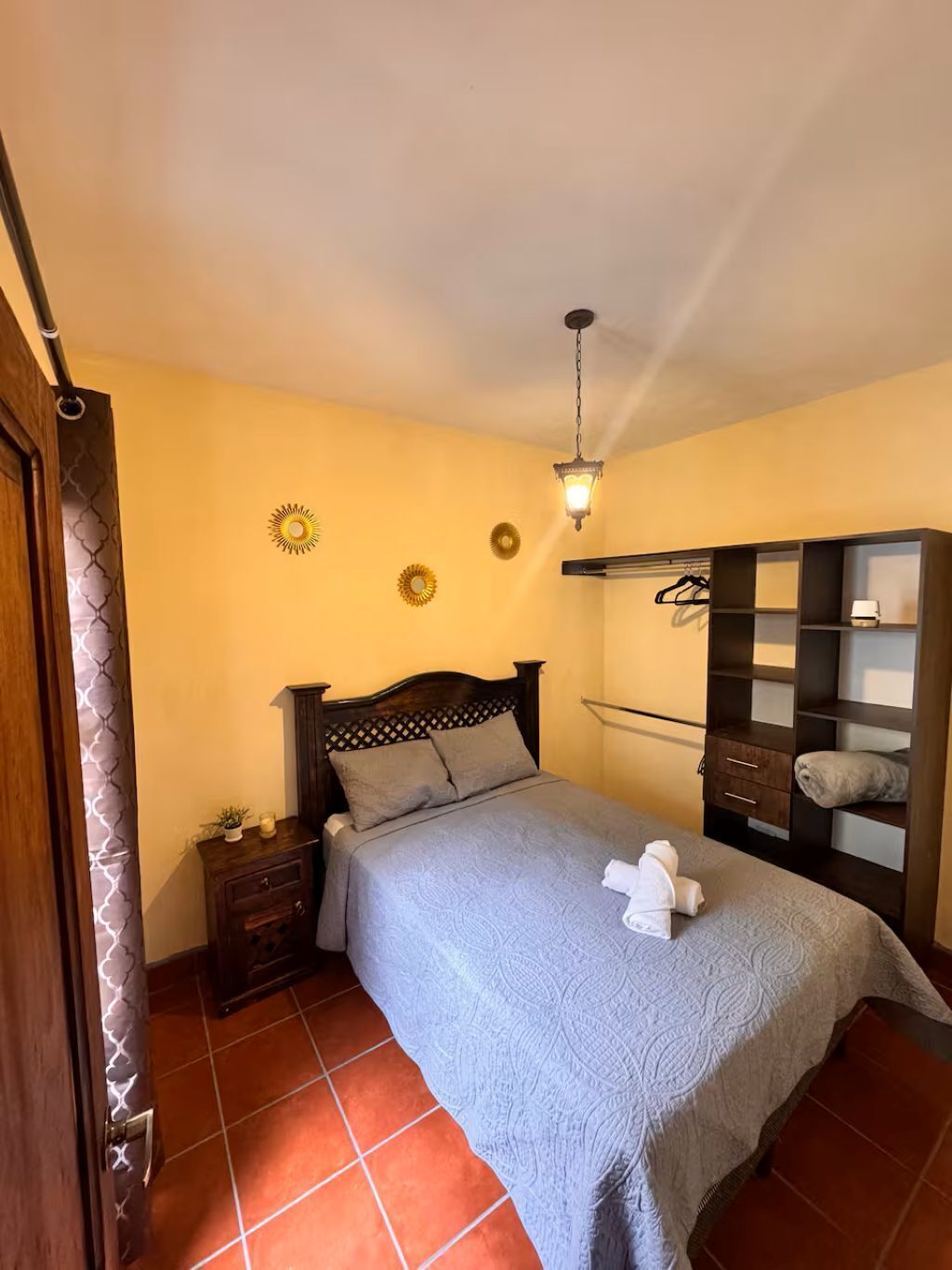 A bedroom with a bed, nightstand, dresser, and a hanging light fixture.
