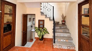 A hallway with a tiled floor, wooden doors, a staircase with patterned tiles, and a potted plant. - Terrace with volcano view/ Colonial Villa + Parking in Antigua Guatemala (Antigua Guatemala)