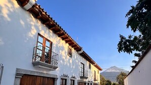 A narrow street with a white building featuring wooden balconies and a mountain in the background. - Terrace with volcano view/ Colonial Villa + Parking in Antigua Guatemala (Antigua Guatemala)