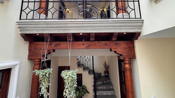 A multi-level interior with a staircase, wooden beams, and hanging plants. - Terrace with volcano view/ Colonial Villa + Parking in Antigua Guatemala (Antigua Guatemala)