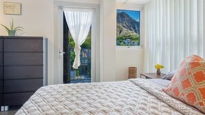 A bedroom with a bed, a dresser, a window with a mountain view, and a door with a curtain. - OCEANSIDE SANCTUARY - Waterfront 2 bed/2bath on Oahu's Gold Coast (Honolulu)