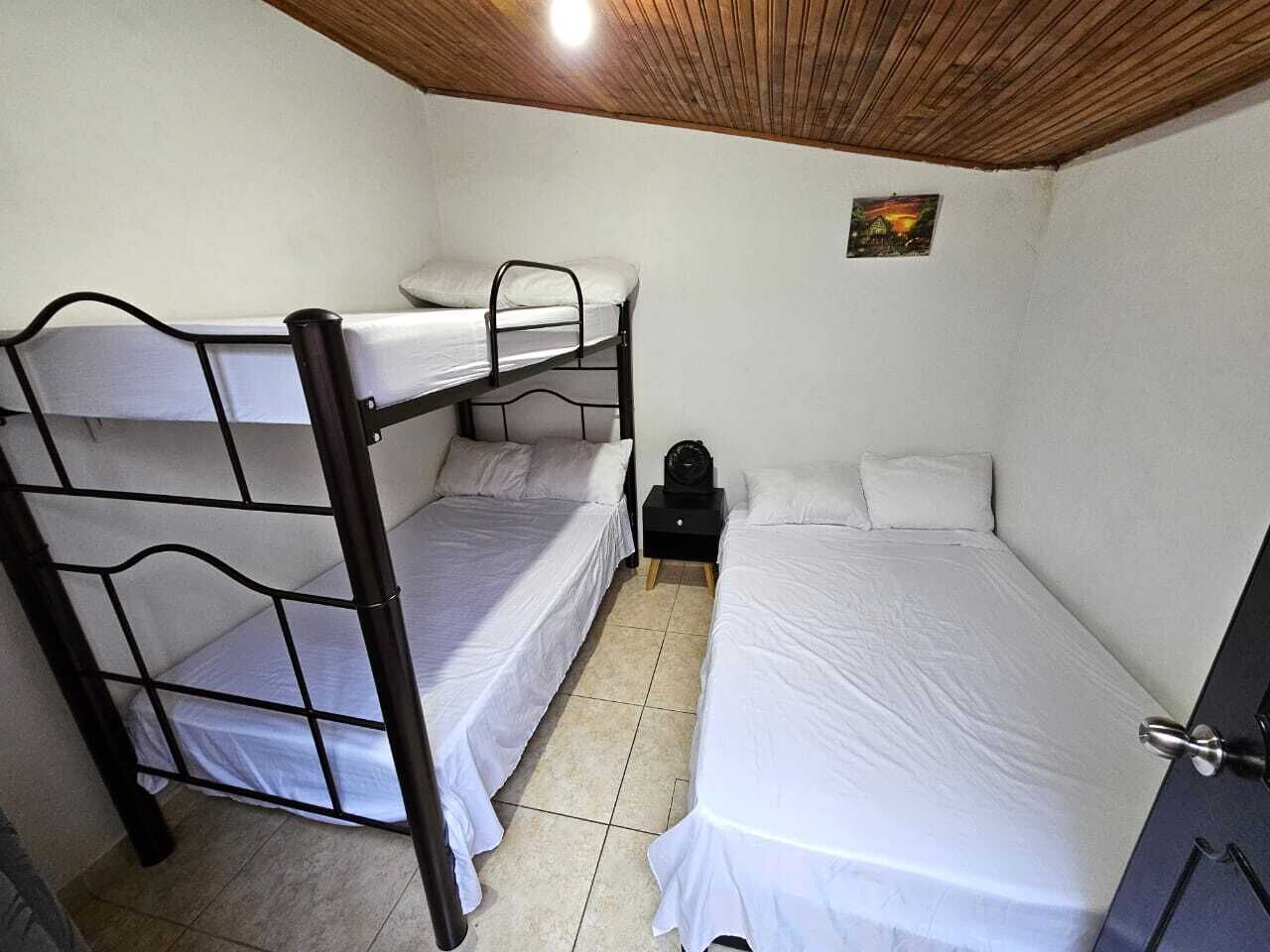 A room with a bunk bed, a single bed, a small table with a lamp, and a door.