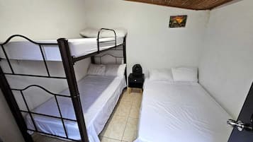 A room with a bunk bed, a single bed, a small table with a lamp, and a door.