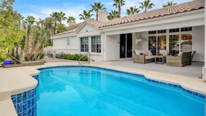 A poolside area with a clear blue pool, outdoor seating, and a white building with a tiled roof. - Quiet 4BR Home w/ Pool Near Summerlin and Strip Central to Everything (Las Vegas)