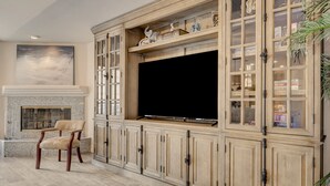A living room with a fireplace, a television, and a cabinet with glass doors. - Quiet 4BR Home w/ Pool Near Summerlin and Strip Central to Everything (Las Vegas)