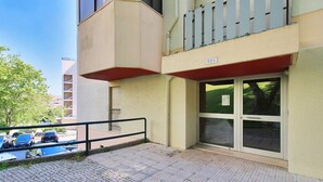 Ein Gebäude mit Eingang im Erdgeschoss, einem Balkon mit Geländer und einer sichtbaren Tür mit Hinweisschild.