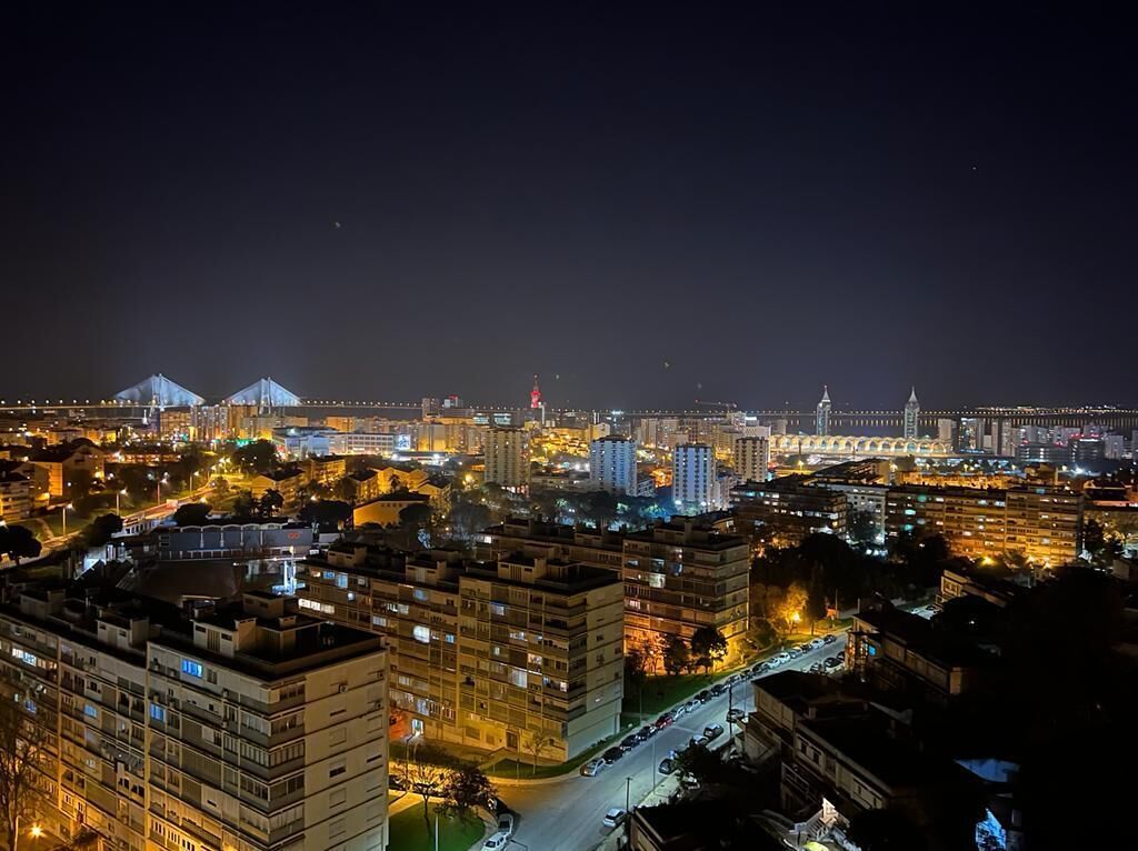 A nighttime cityscape with illuminated buildings, a bridge, and a distant mountain peak.
