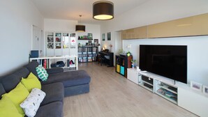 Ein Wohnzimmer mit grauem Sofa, einem Flachbildfernseher, einem Bücherregal und einem Essbereich.