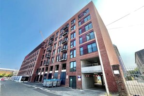 A multi-story building with a brick facade, multiple balconies, and a parking area with covered parking spaces. - Stylish 2BDR City Apartment In Liverpool (Liverpool)