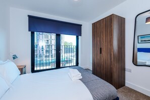 A hotel room with a large bed, a wardrobe, a window with a view of the city, and a bedside lamp. - Stylish 2BDR City Apartment In Liverpool (Liverpool)