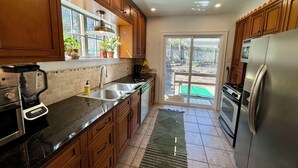 A kitchen with wooden cabinets, a stainless steel refrigerator, a built-in oven, and a window with potted plants. - Sunny, safe, walkable house with King bed and AC (Kansas City)