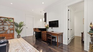 Ein modernes Zimmer mit Schreibtisch aus Holz, zwei Stühlen, einem Fernseher, einer Topfpflanze und einem dekorativen Schrank.