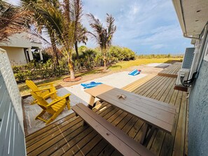 A wooden deck with a table and chairs, a covered area with a blue mat, and a view of the beach and palm trees. - BEACHHOUSE #1 Mermaids Paradise-full kitchen, private oceanfront patio 1st floor (Melbourne Beach)