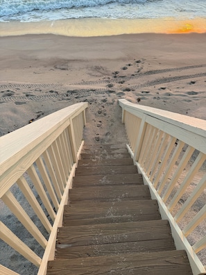 A wooden staircase leading to a beach with footprints in the sand.