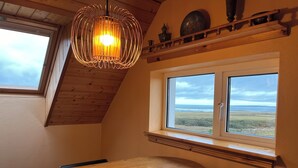 Ein Essbereich mit Holztisch und -stühlen, einer Pendelleuchte, einem Fenster mit Meerblick und einer Holzzieldecke.