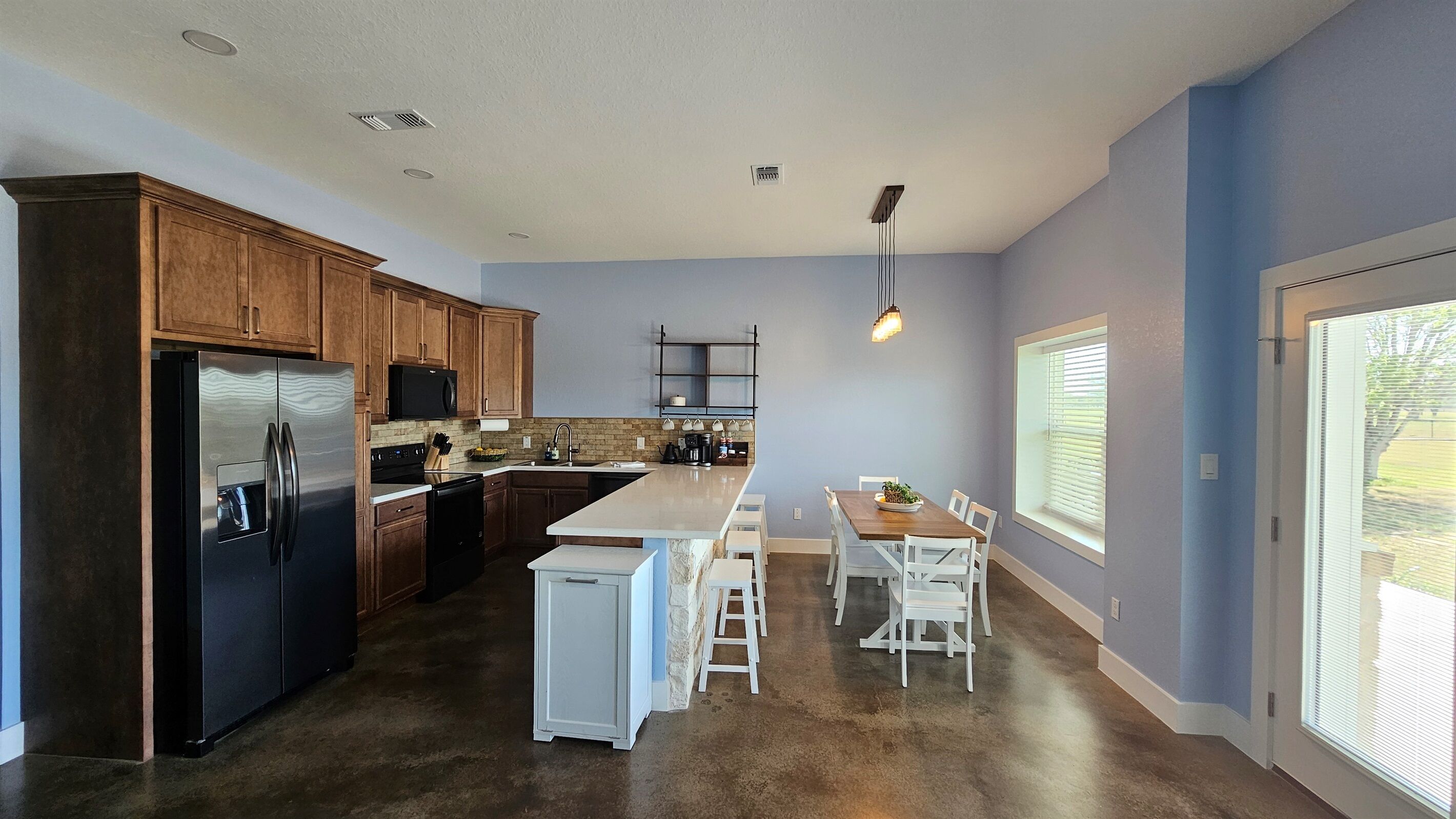 A modern kitchen with a central island, wooden cabinets, stainless steel appliances, and a dining area with white chairs.