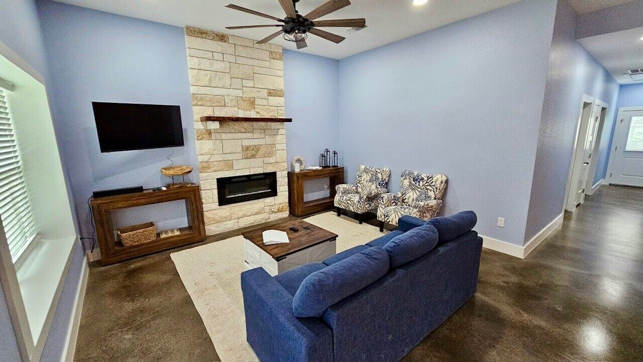 A living room with a stone fireplace, a blue sofa, a television, and a ceiling fan.