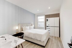 A modern hotel room with a bed, bedside table, lamp, and a view of the city through the window.