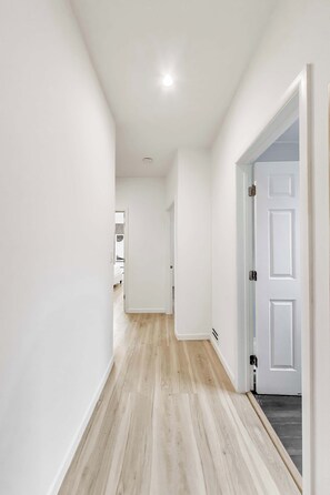 A hallway with white walls, a wooden floor, and a white door.