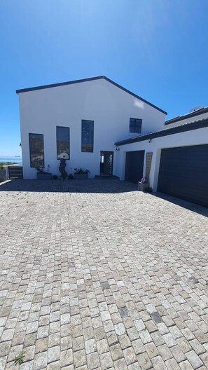 Une maison moderne à deux étages, dotée d’une allée pavée et d’un garage.