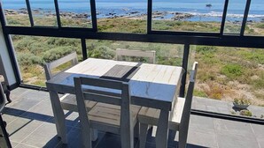 A patio with a table and chairs, a view of the ocean, and a grassy area. - Mystic Falls Apartment on the Bay (St. Helena Bay)