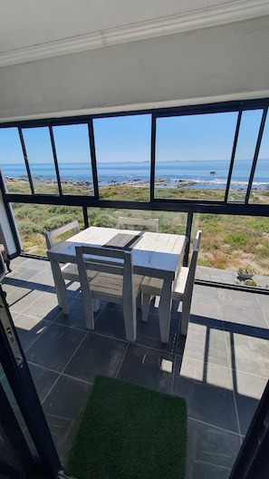 Un patio con mesa y sillas, vista al océano y una zona ajardinada.