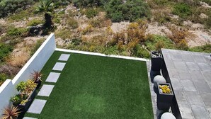 A patio with artificial grass, a stone pathway, and planters with yellow flowers. - Mystic Falls Apartment on the Bay (St. Helena Bay)
