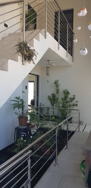 Un interior moderno con una escalera, barandillas de metal, plantas en macetas e iluminación colgante.