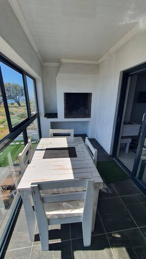 Une terrasse avec une table et des chaises blanches, une cheminée et une vue sur l’extérieur.