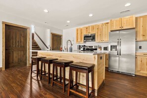 Una cocina moderna con armarios de madera, electrodomésticos de acero inoxidable y una isla central con taburetes de bar.