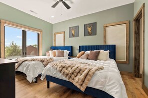 Un dormitorio con dos camas, ventilador de techo y ventanas amplias con persianas.