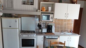Cozinha compacta com geladeira, fogão, micro-ondas e pia. Há uma mesa de jantar com cadeiras e uma tigela sobre ela.