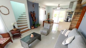 A modern living room with a sofa, a coffee table, a chair, a staircase, and a kitchen area. - Caribbean getaway, private terraces, 2 minutes from the beach (Puerto Aventuras)