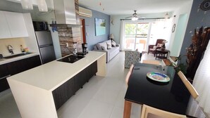 A modern kitchen with a central island, a dining area with a table and chairs, and a living area with a sofa and a TV. - Caribbean getaway, private terraces, 2 minutes from the beach (Puerto Aventuras)