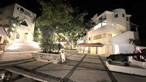 A modern hotel with a well-lit entrance, a stone pathway, and a parked vehicle. - Caribbean getaway, private terraces, 2 minutes from the beach (Puerto Aventuras)
