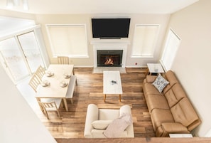 Ein Wohnzimmer mit Kamin, einer Couch, einem Esstisch und einem Fernseher, der über dem Kamin angebracht ist.