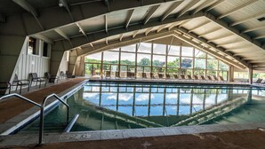 An indoor swimming pool with clear water, a roofed structure, and a view of greenery outside. - Lakeside Living at Abbey Springs - Pools & Beach! (Fontana)