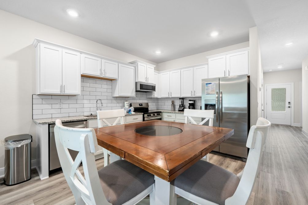 A modern kitchen with white cabinets, a stainless steel refrigerator, and a wooden dining table.