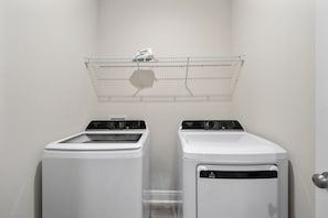 A laundry area with two white washing machines, a metal drying rack, and a door with a handle. - Marigold House: Foley (Foley)