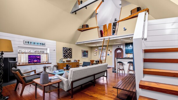 A spacious living area with a high ceiling, wooden flooring, a sofa, a coffee table, and a TV. - *NEW* Historic Ptown Cottage - Dogs Welcome, Deck, Parking, Vibrant and Colorful (Provincetown)