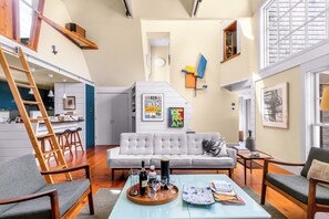 A modern living space with a loft area, a dining area, and a kitchen. - *NEW* Historic Ptown Cottage - Dogs Welcome, Deck, Parking, Vibrant and Colorful (Provincetown)